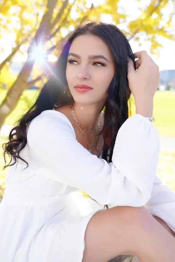 A young woman poses in a white dress in the sunlight