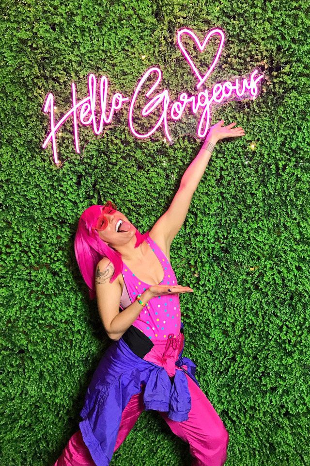 A woman posing inform of a booth backdrop that says gorgeous