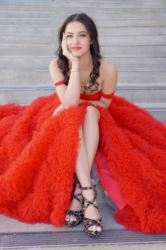 A young woman sits cross-legged in a red dress on steps